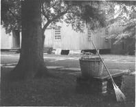 SA0390 - Photo of a large building and a basket and rake on a stone seat under a tree., Winterthur Shaker Photograph and Post Card Collection 1851 to 1921c